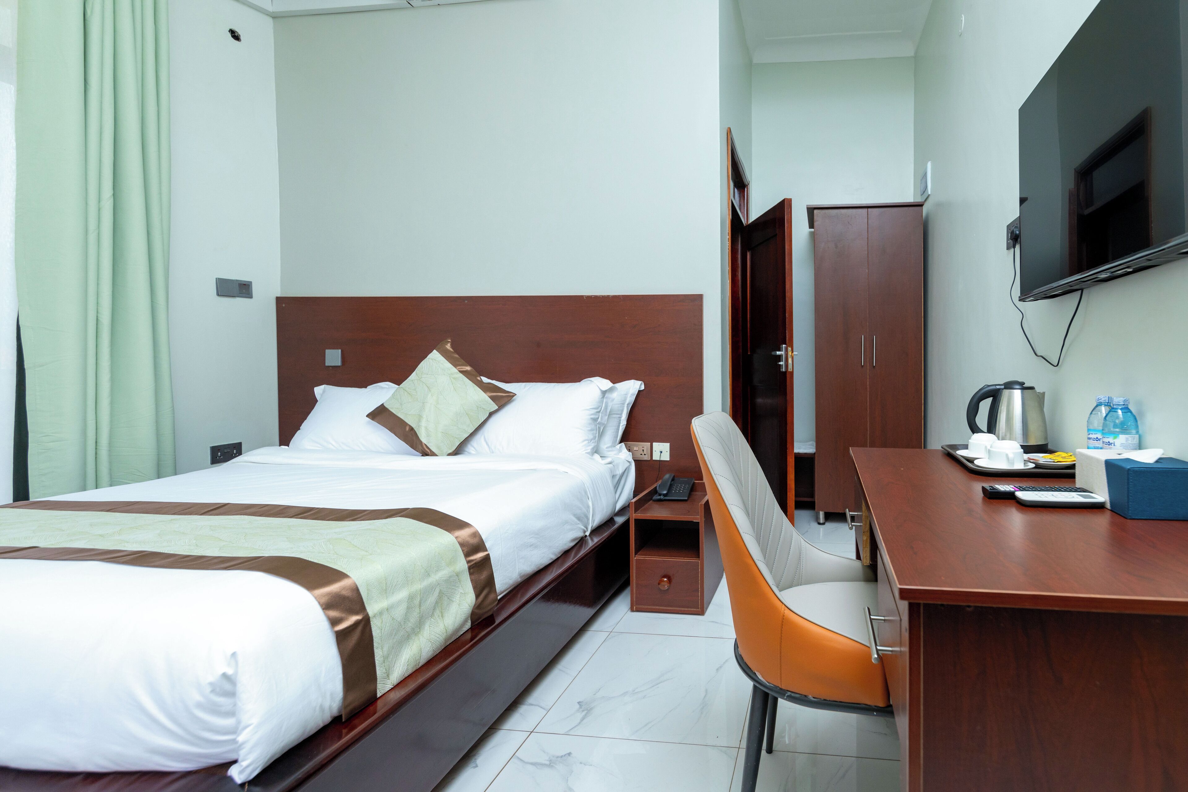 A hotel room with a bed, a desk, a chair, a television, and a wardrobe.