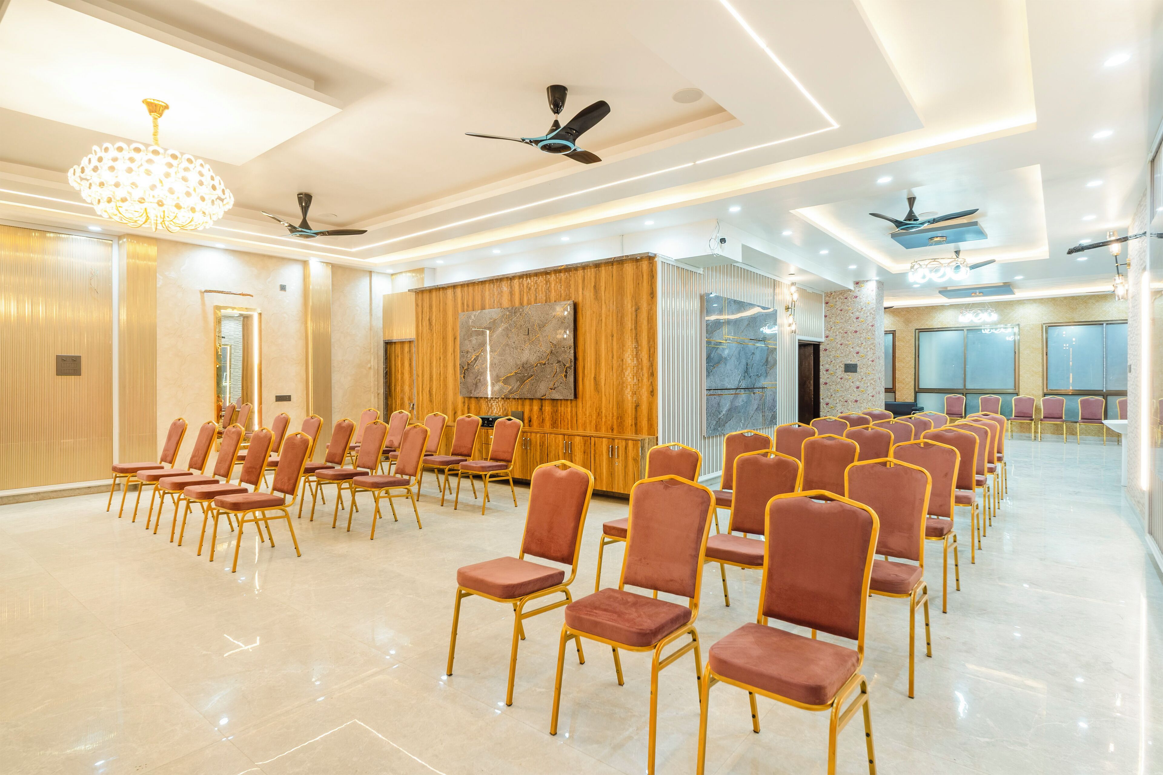A conference room with rows of chairs, ceiling fans, and a large screen.