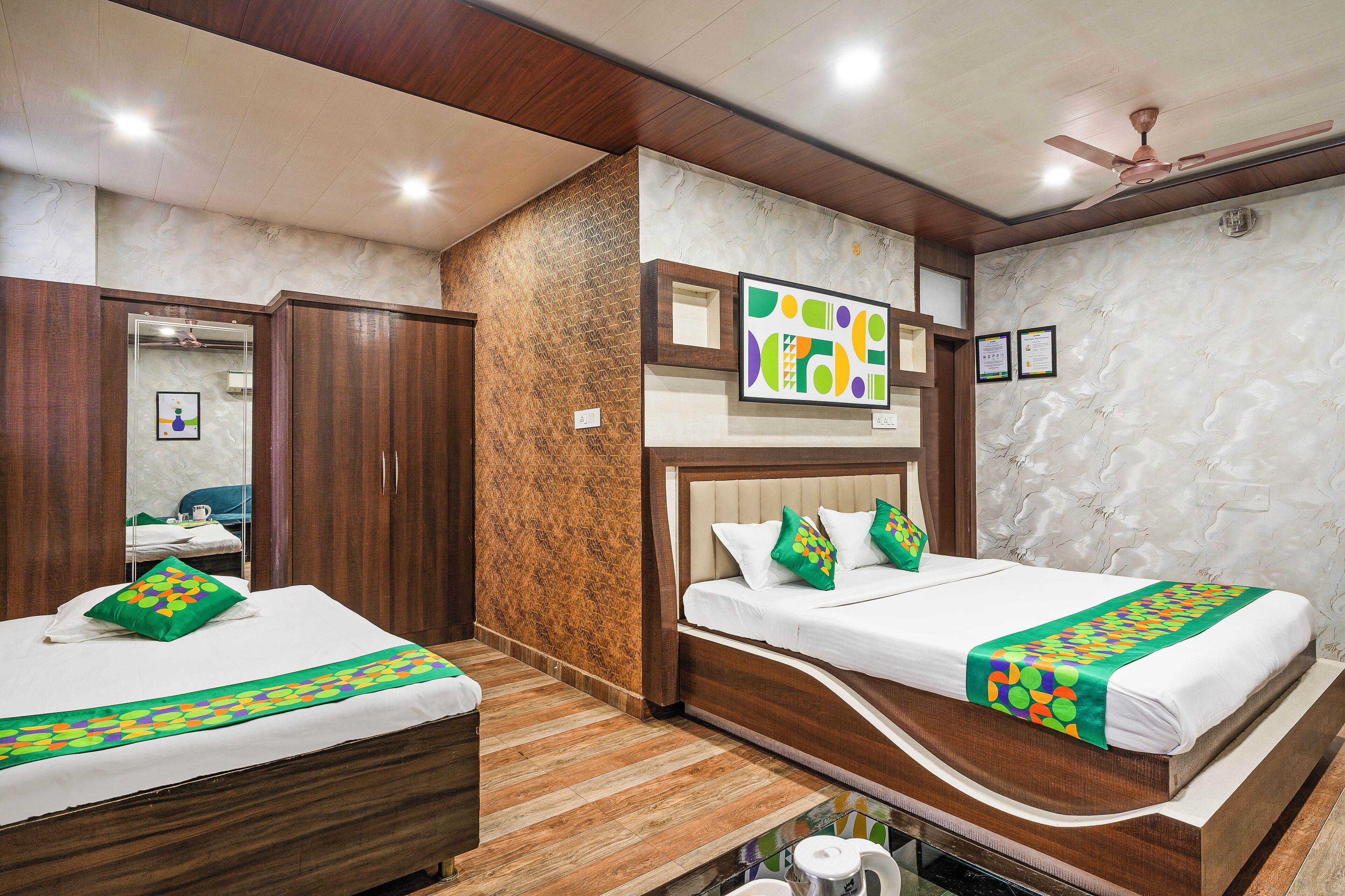 A hotel room with two beds, wooden flooring, a ceiling fan, and a decorative wall.