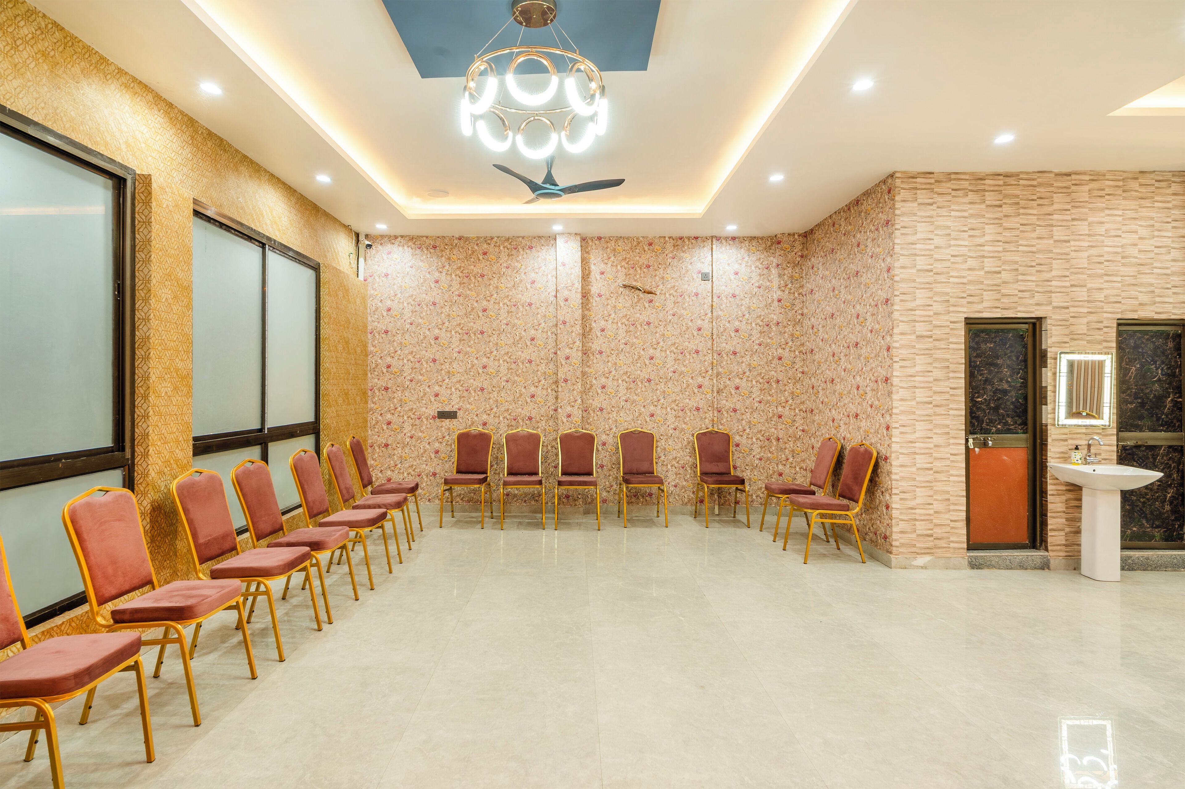Un salón de conferencias con filas de sillas, un ventilador de techo y un lavamanos en la pared.