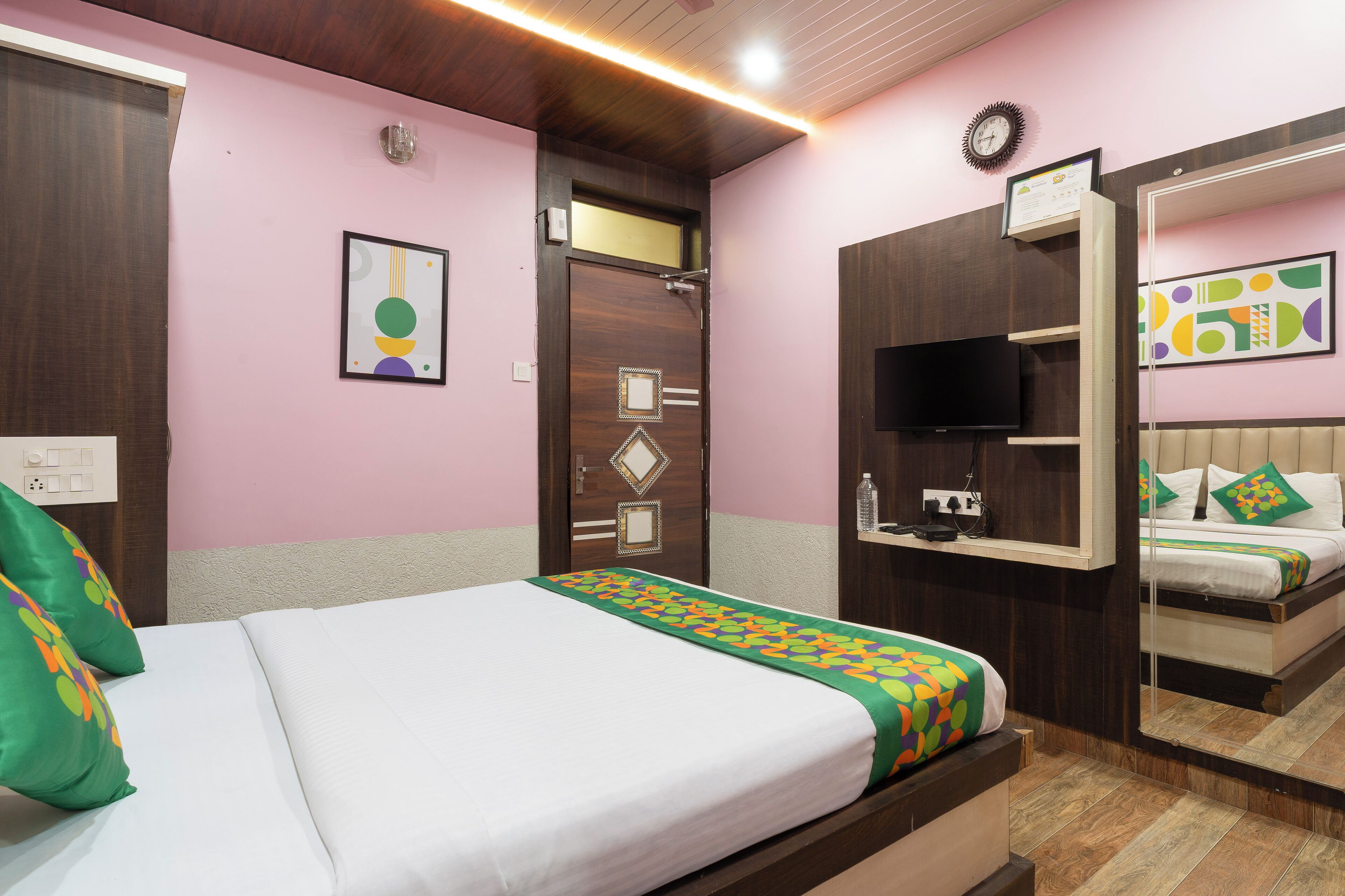 A hotel room with a bed, a television, a mirror, and a door with a decorative panel.
