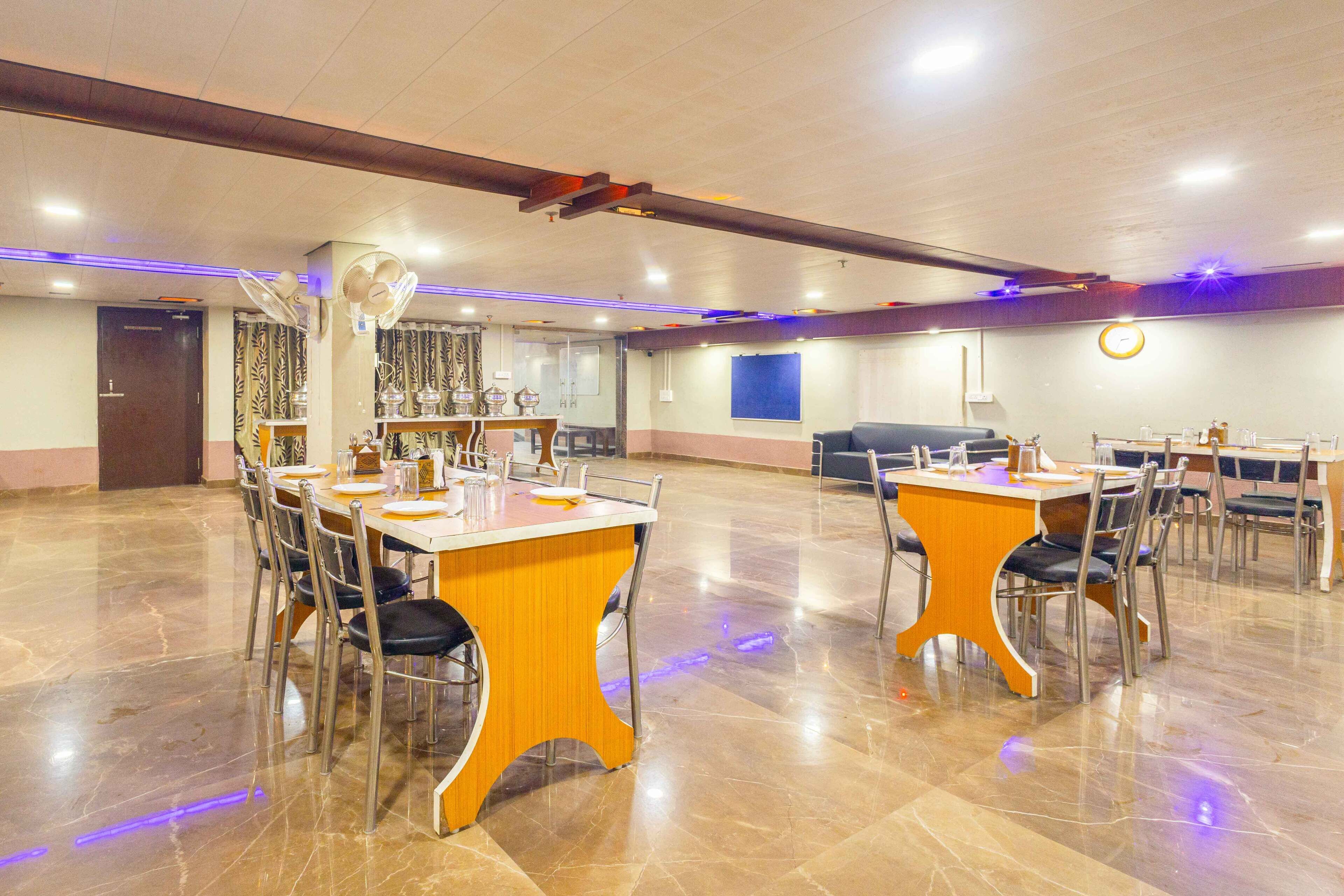 Une salle de conférence spacieuse, dotée de plusieurs tables et chaises, et équipée de ventilateurs de plafond et d’une horloge murale.