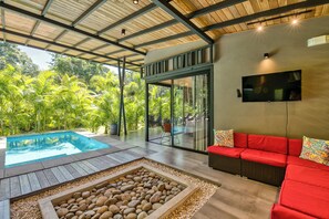 Un espace piscine intérieur moderne avec un mur en verre, un canapé rouge et un téléviseur fixé au mur.