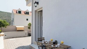 Un patio con una mesa lista para dos, asientos exteriores y vista a un edificio con techo de tejas rojas.