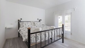 Un dormitorio con cama, mesita de noche, ventana con cortinas translúcidas y lámpara en el techo.