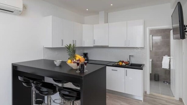 Una cocina moderna con armarios blancos, una isla negra con taburetes y un frutero.