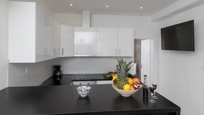 Una cocina moderna con armarios blancos, encimera negra y un frutero con una botella y vasos.