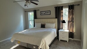 Une chambre à coucher avec un lit, une table de chevet, un ventilateur de plafond et une fenêtre avec des rideaux.