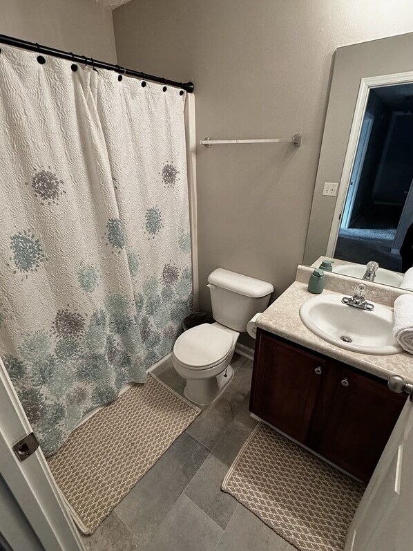 Ein Badezimmer mit Duschvorhang, Toilette, Waschbecken und Spiegel.