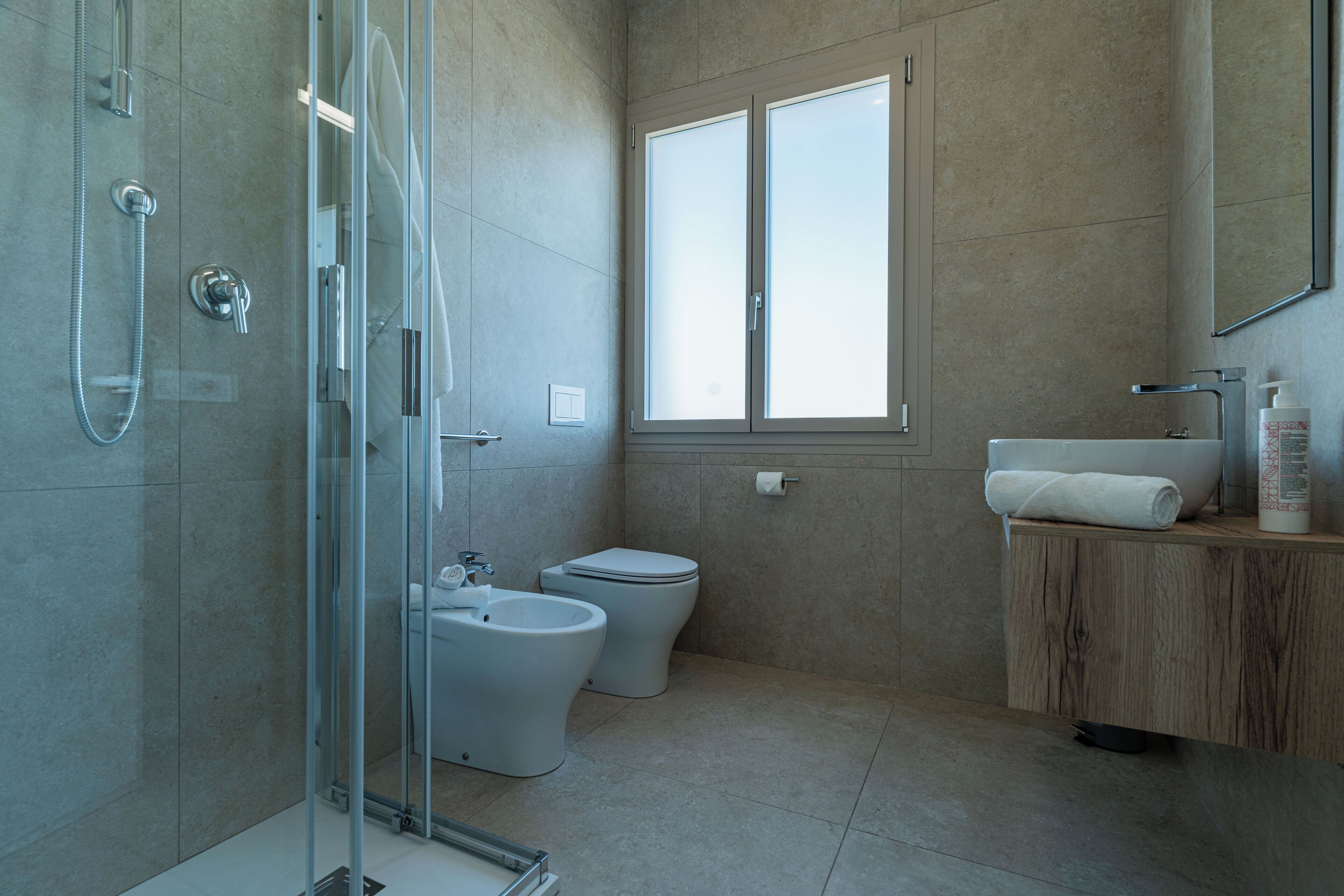 A modern bathroom with a glass shower enclosure, a toilet, bidet, and a vanity with a mirror.