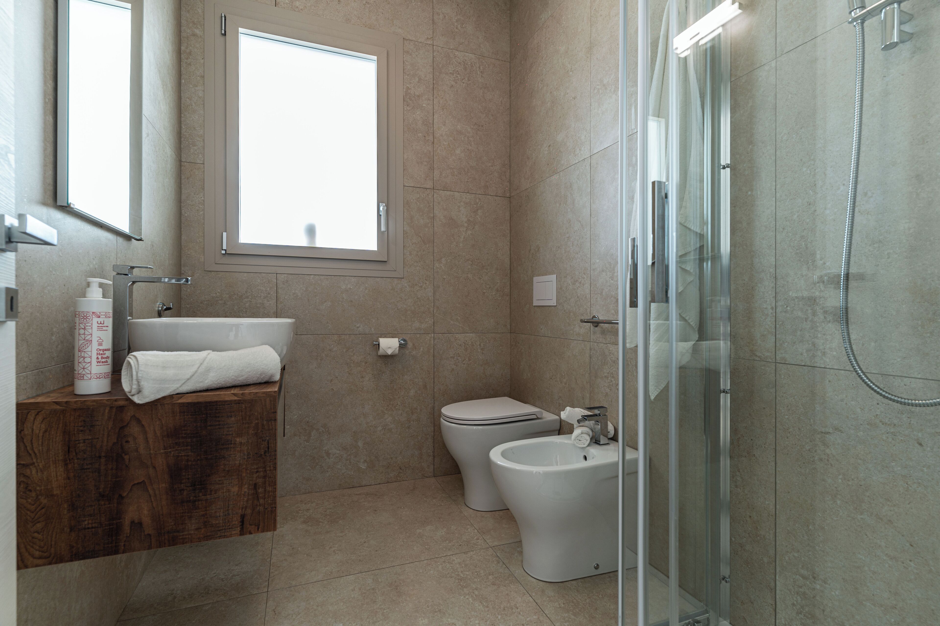 A modern bathroom with a wooden vanity, a toilet, a bidet, and a glass-enclosed shower.