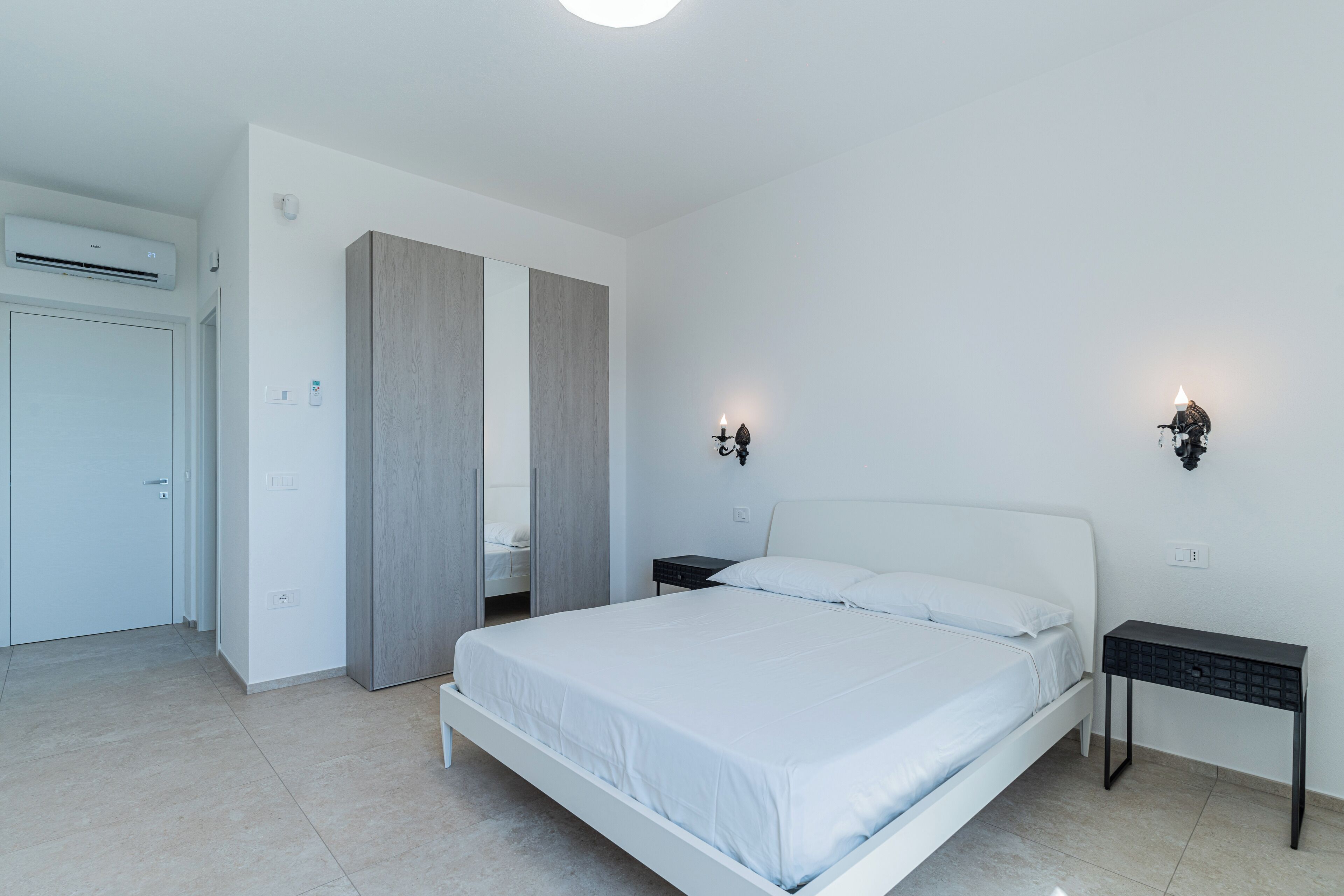 A modern bedroom with a white bed, a nightstand, and a wall-mounted light.
