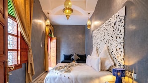 Ein Schlafzimmer mit einem großen Bett, einem Nachttisch, einer dekorativen Wandverkleidung und einer Kronleuchter.