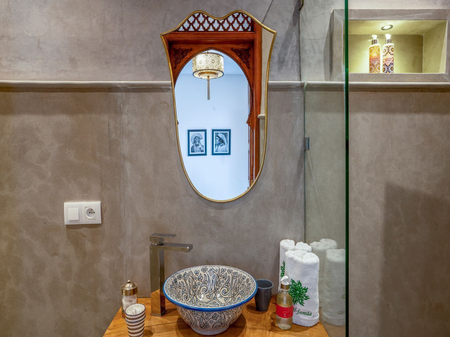 A bathroom with a round mirror, a sink with a patterned bowl, a towel rack, and a shelf with toiletries.