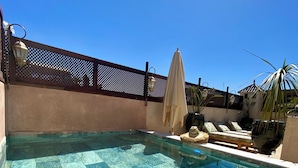 Ein klares, blaues Schwimmbecken mit Fliesenboden, Liegestühlen und einer Pergola mit Sonnenschirmen.