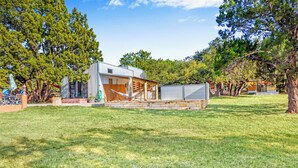 Una casa moderna con una amplia terraza, rodeada por un césped cuidado y árboles.