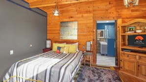 Un dormitorio con cama, techo de madera, televisor y baño visible a través de una puerta abierta.