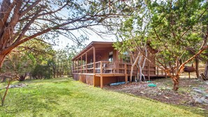 Een houten chalet met een terras, omringd door bomen en een gazon.