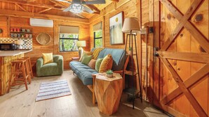 Een knus interieur van een chalet met een houten plafond, een bank met kussens, een salontafel, een bar met krukken, en een grote houten deur.