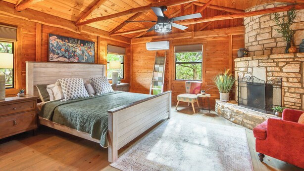 Een slaapkamer in een blokhut met een bed, een rode stoel, een open haard en een plafondventilator.