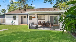 Een woonhuis met een overdekte patio, buitenmeubels en een omheinde tuin.