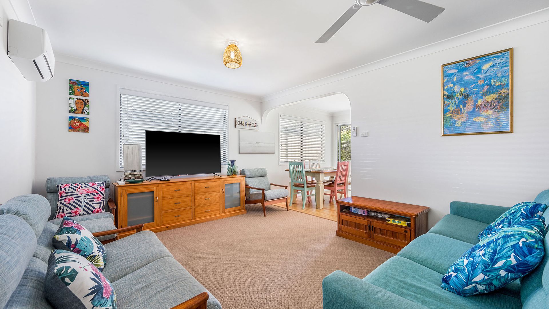A living room with a flat-screen TV, wooden cabinet, and a dining area with chairs and a table.