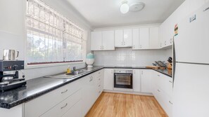 A modern kitchen with white cabinetry, a stainless steel sink, a built-in oven, and a coffee machine. - Mirrabooka - Charming 2-bedroom holiday house (Lake Cathie)