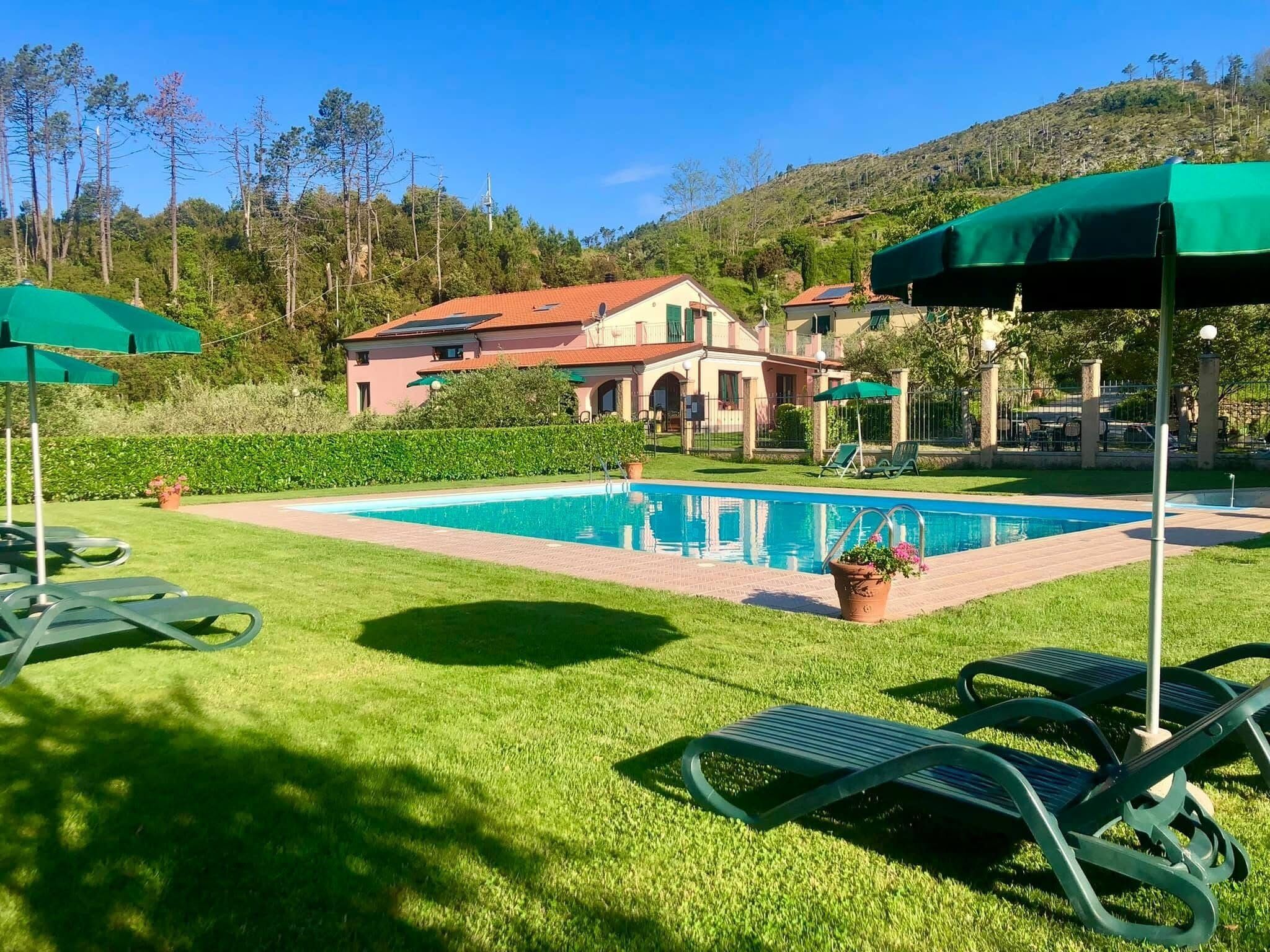 A swimming pool with lounge chairs and umbrellas, surrounded by a well-maintained lawn and a building with a red roof.
