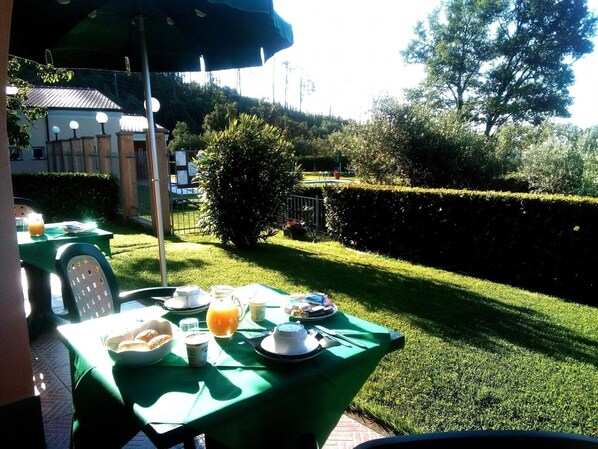An outdoor dining area with a table set for breakfast, surrounded by well-manicured hedges and trees.