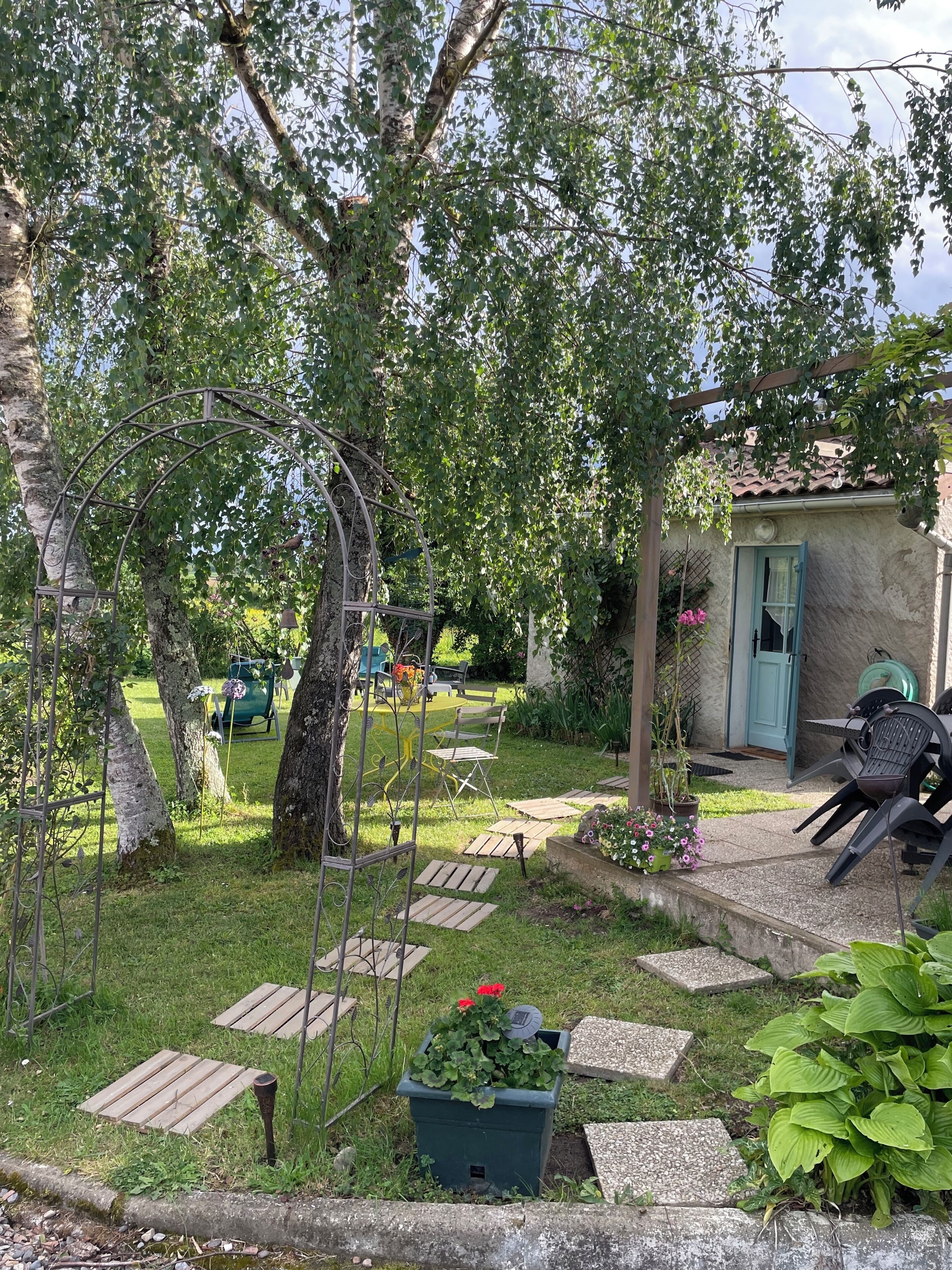 Un giardino con una pergola, un'area salotto all'aperto e un piccolo edificio con una porta blu.