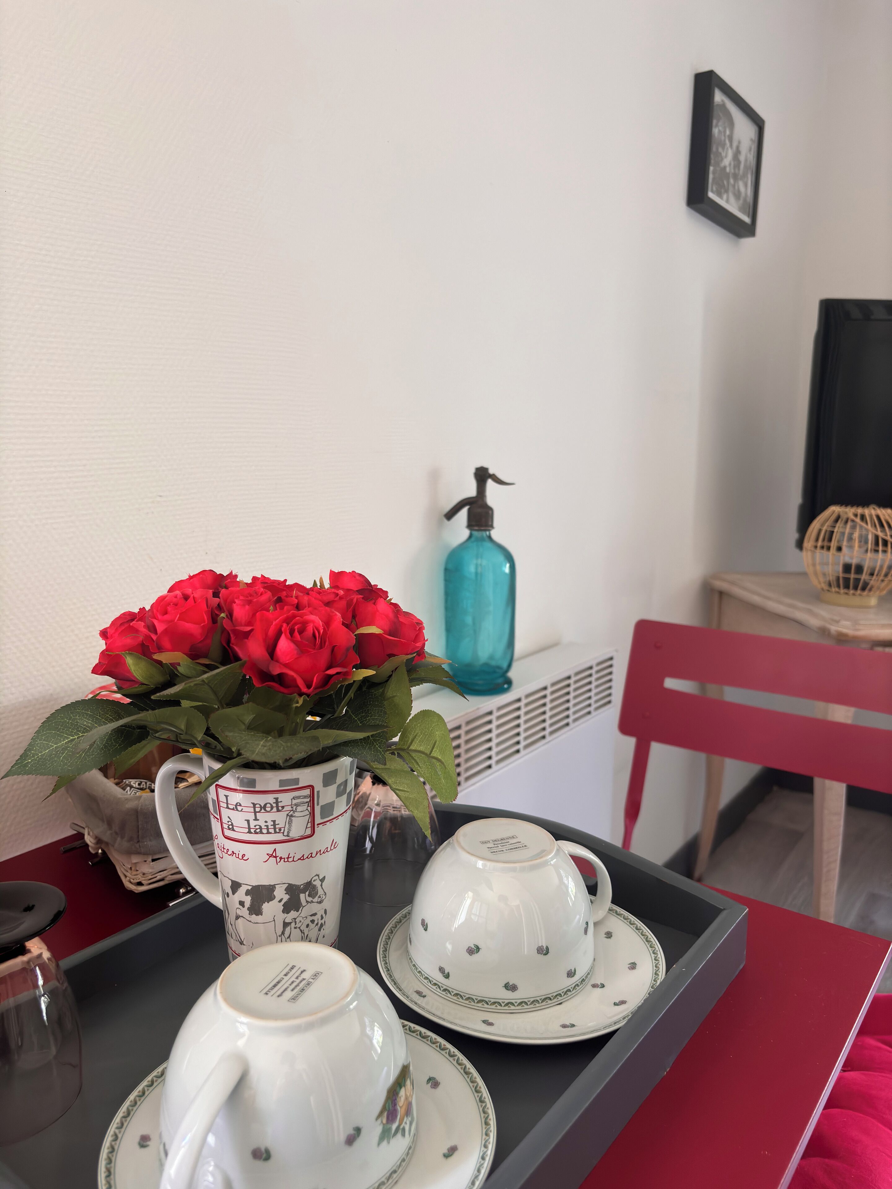 A tray with a white teapot, two teacups, and a vase of red roses on a table.