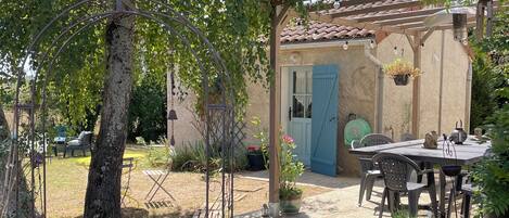 A garden with a pergola, a table and chairs, and a small building with a blue door.
