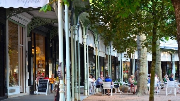 A café with outdoor seating, white chairs, and a covered area with columns.