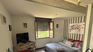 Una habitación pequeña con cama, escritorio, televisor y ventana con persianas.
