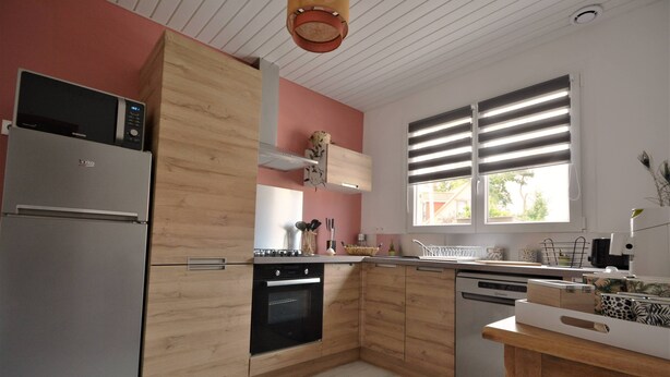 A modern kitchen with wooden cabinets, stainless steel appliances, and a window with blinds. - Renovated house located 5 minutes from the beach and playground, close to shops. (Le Crotoy)