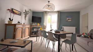 A dining area with a table and chairs, a television on a stand, and a window with curtains. - Renovated house located 5 minutes from the beach and playground, close to shops. (Le Crotoy)