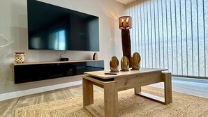Un soggiorno moderno con una TV a schermo piatto fissata al muro, un tavolino in legno con oggetti decorativi e un'elegante lampada da terra.