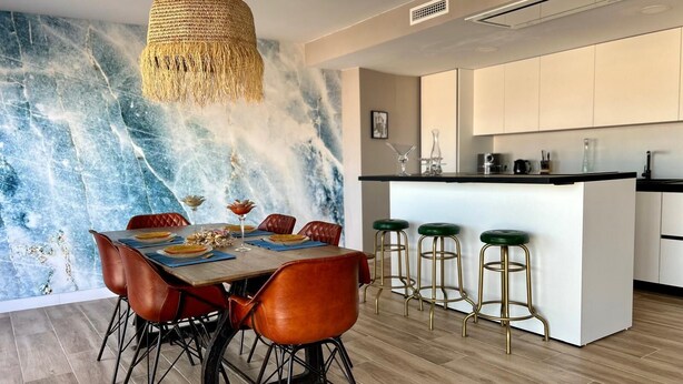 Una cucina moderna con rivestimento in marmo, un'area pranzo con poltrone in pelle e un bancone con sgabelli.