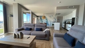 Un soggiorno moderno con un divano grigio, un tavolino da caffè e vista sulla città attraverso ampie finestre.