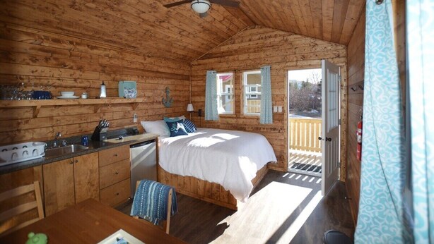 Una cabaña acogedora con interior de madera, una cama, una pequeña cocina y un balcón con vistas.