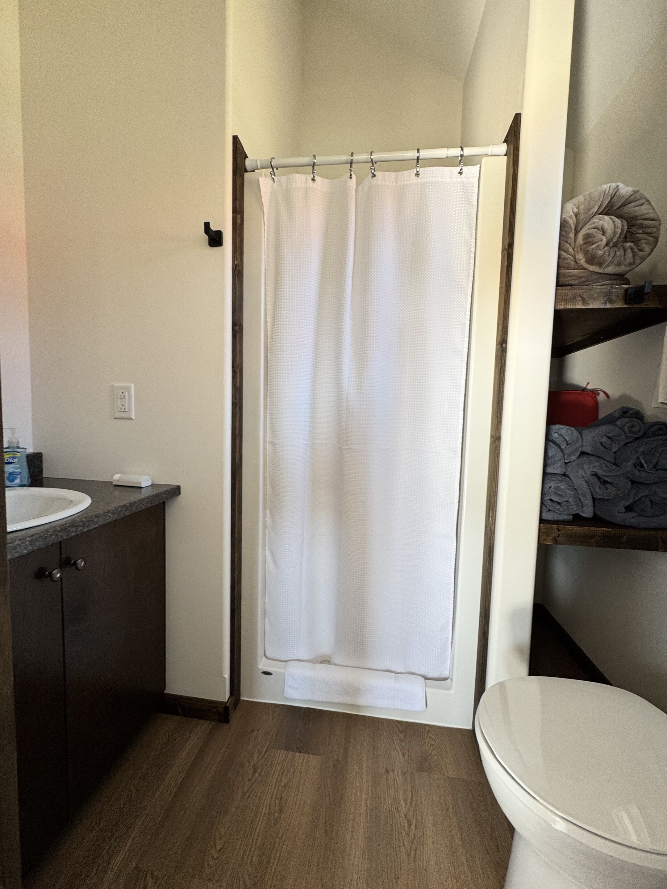 A bathroom with a shower curtain, a toilet, a sink, and a shelf with towels.