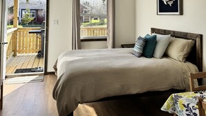 Un dormitorio con cama, ventilador de techo, ventana con cortinas, terraza de madera afuera y un cuadro en la pared.