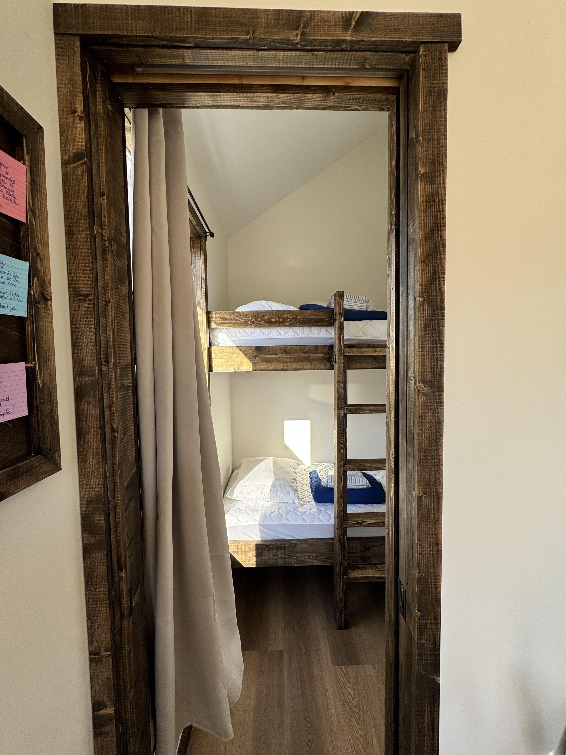 Une chambre avec un lit superposé, une porte en bois, un rideau et un interrupteur fixé au mur.