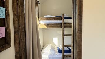 Une chambre avec un lit superposé, une porte en bois, un rideau et un interrupteur fixé au mur.