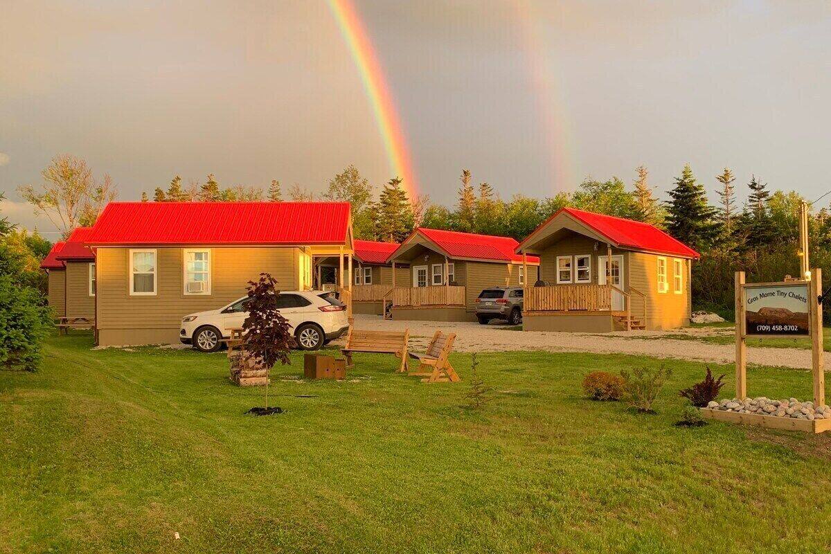 Una hilera de cabañas con techos rojos, un césped y un letrero que dice 'Cottage Home Tiny Chalet'.
