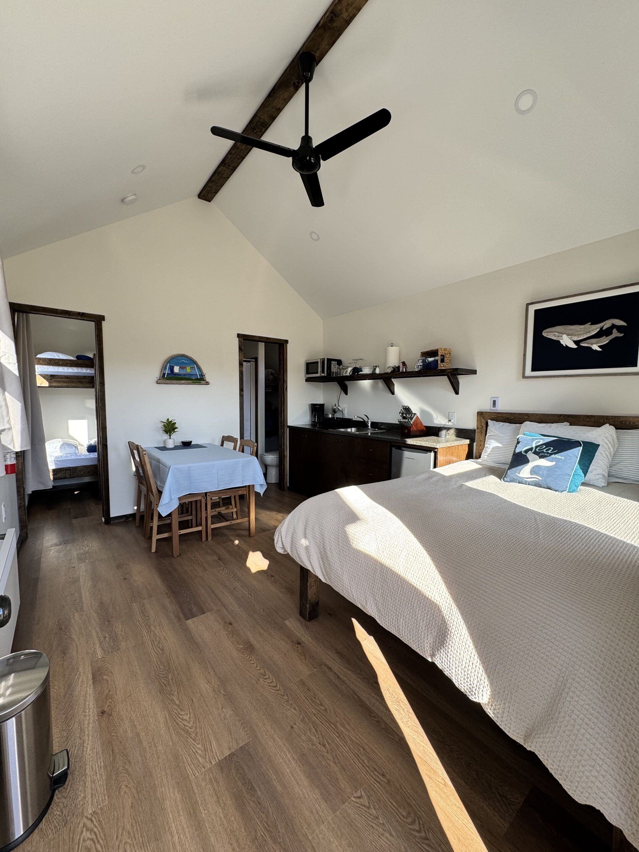A bedroom with a bed, a ceiling fan, a dining area with a table and chairs, and a kitchen area with a microwave and cabinets.
