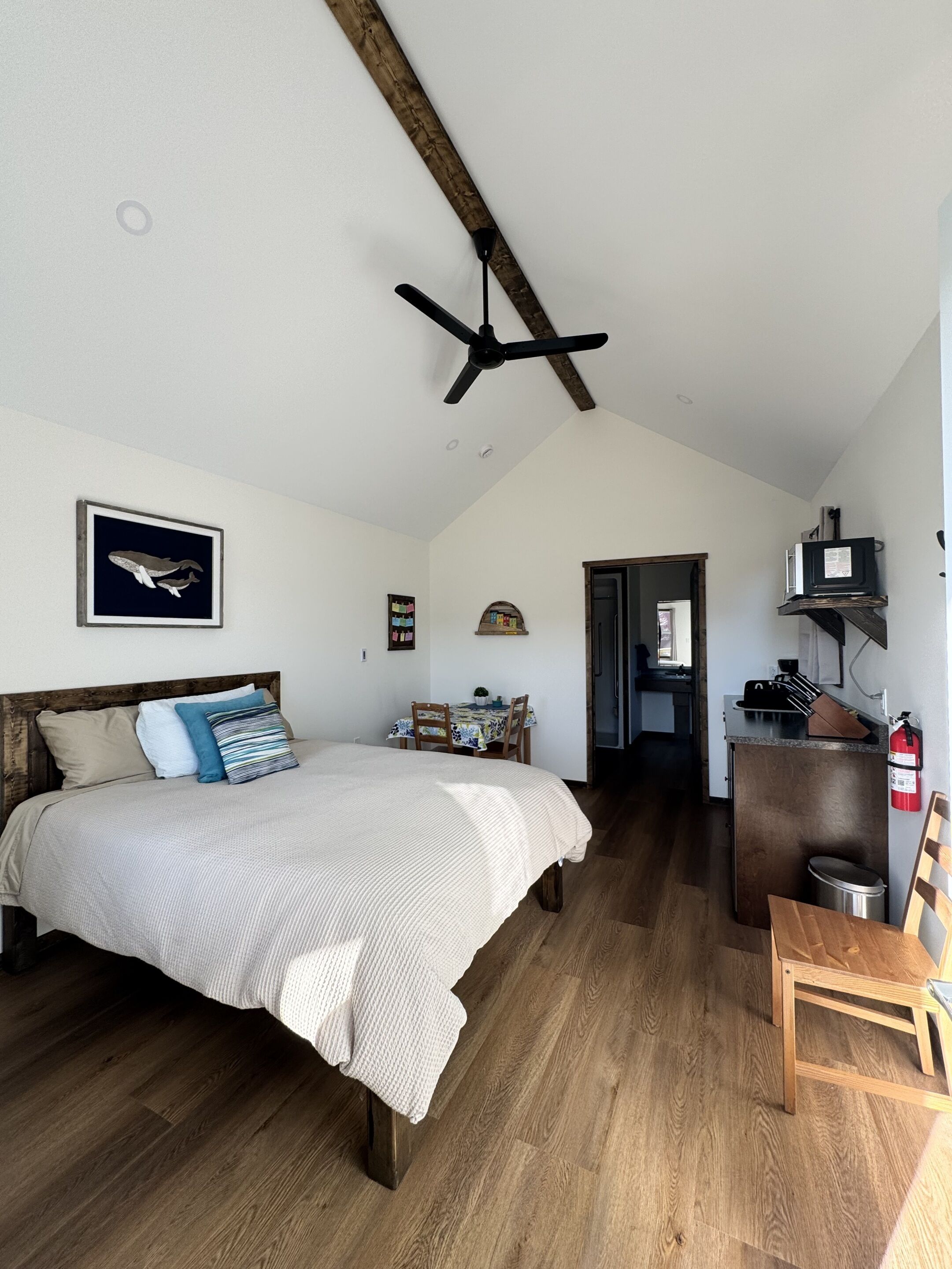 Une chambre avec un lit, un plancher en bois, un ventilateur de plafond et une vue sur la cuisine.