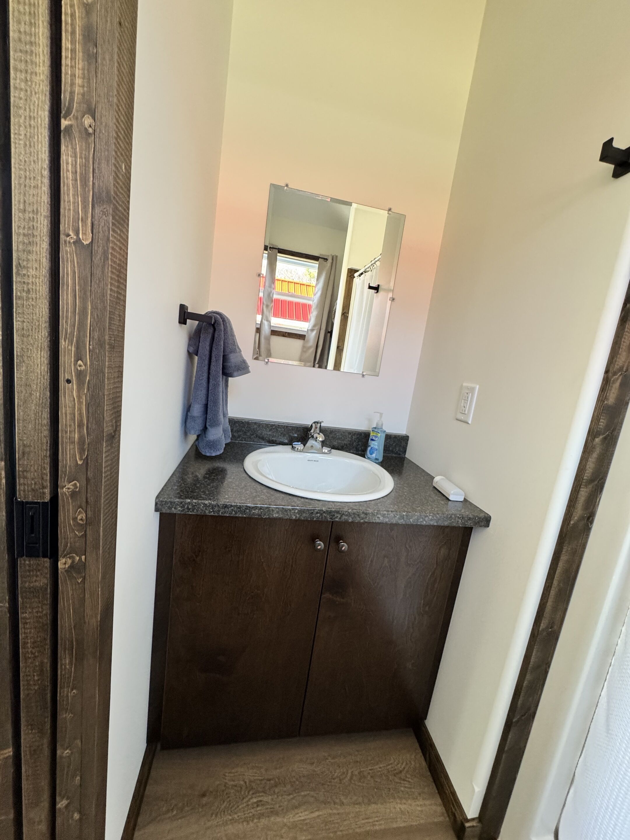A bathroom with a wooden vanity, a white sink, a mirror, and a towel hanging on the wall.