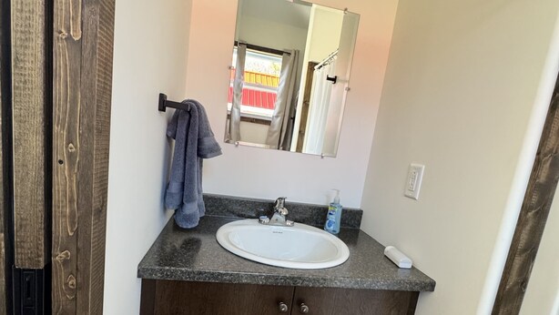A bathroom with a wooden vanity, a white sink, a mirror, and a towel hanging on the wall. - Gros Morne Tiny Chalets (Rocky Harbour)