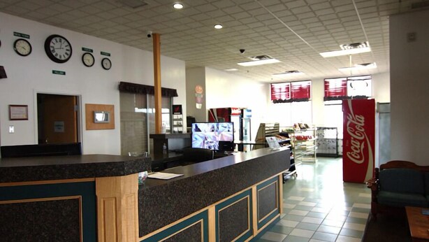 A reception area with a counter, clocks, a Coca-Cola refrigerator, and a seating area. - Western Budget Plus Killam Krossing (Killam)